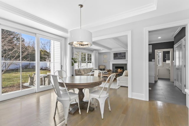 dining area featuring a warm lit fireplace, wood finished floors, visible vents, baseboards, and ornamental molding