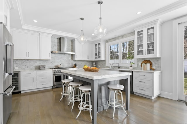 kitchen featuring a kitchen breakfast bar, white cabinets, wall chimney range hood, appliances with stainless steel finishes, and dark wood-style floors