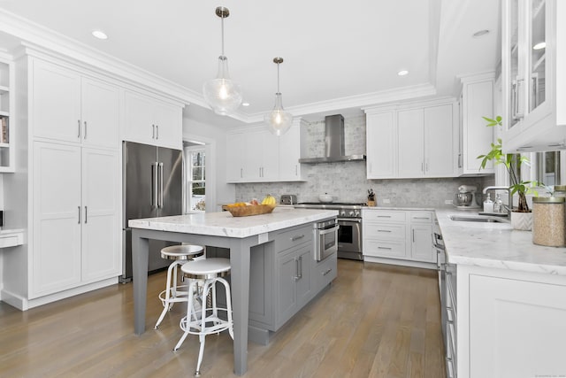 kitchen with premium appliances, gray cabinetry, a sink, a center island, and wall chimney exhaust hood