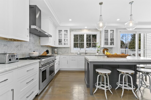 kitchen with crown molding, decorative backsplash, wall chimney range hood, double oven range, and a kitchen breakfast bar