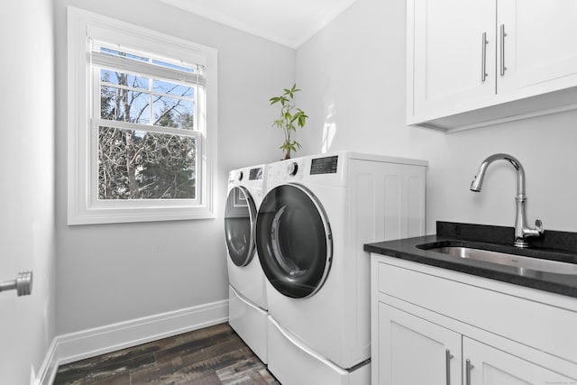 clothes washing area with dark wood-style flooring, washing machine and clothes dryer, cabinet space, a sink, and baseboards