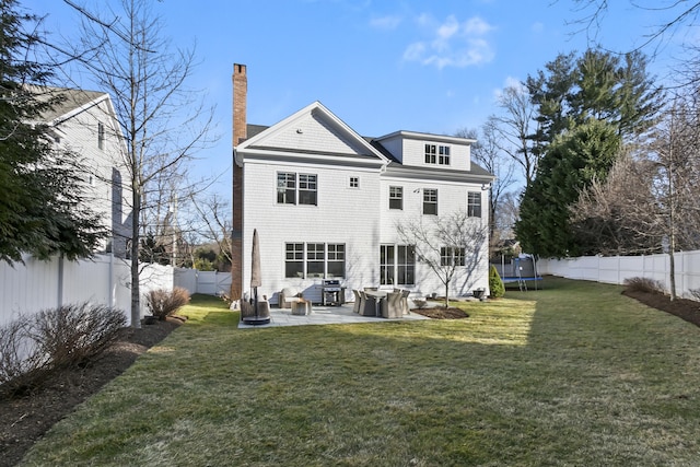 rear view of house with a trampoline, a yard, a chimney, a patio, and a fenced backyard