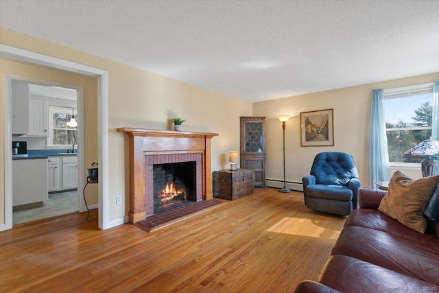 living room with a brick fireplace, plenty of natural light, light wood-style floors, and a baseboard radiator