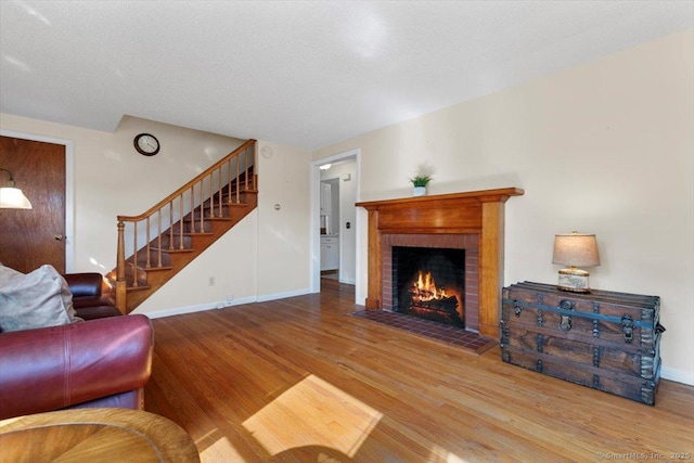 living room with baseboards, stairway, wood finished floors, and a brick fireplace