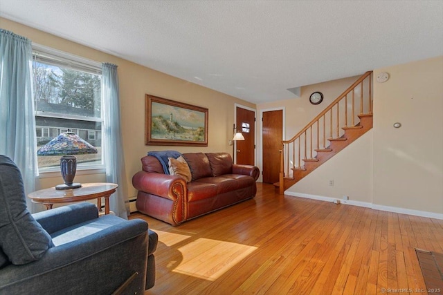 living room with a textured ceiling, baseboards, light wood-style flooring, and stairs