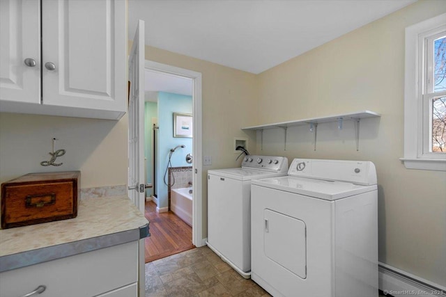 clothes washing area featuring baseboard heating, baseboards, cabinet space, and washing machine and clothes dryer
