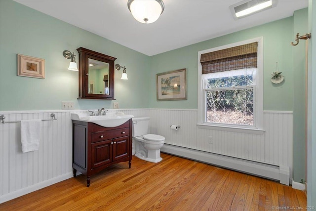 bathroom featuring vanity, hardwood / wood-style floors, baseboard heating, and wainscoting