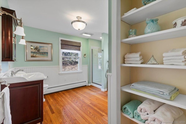 full bath with a baseboard heating unit, vanity, a stall shower, a wainscoted wall, and wood finished floors