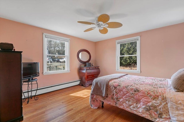 bedroom featuring a ceiling fan, multiple windows, wood finished floors, and a baseboard radiator