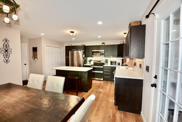 kitchen with light wood-style flooring, a kitchen island, light countertops, appliances with stainless steel finishes, and backsplash