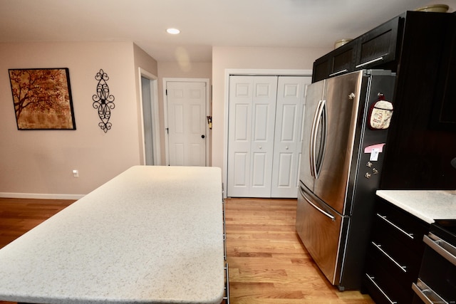 kitchen with light wood-type flooring, freestanding refrigerator, a center island, and dark cabinets