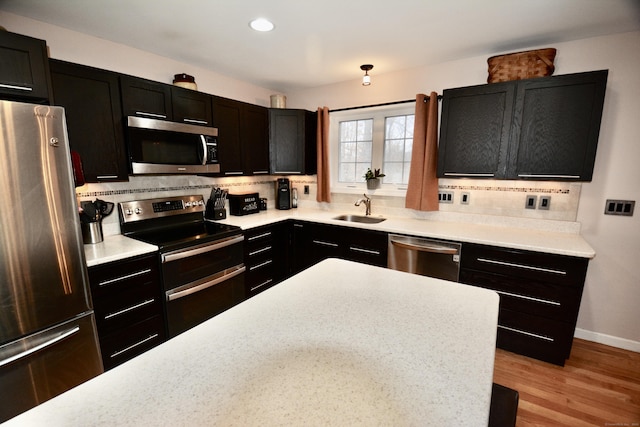 kitchen featuring stainless steel appliances, dark cabinetry, a sink, and tasteful backsplash