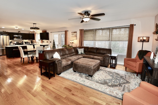 living room with light wood finished floors, a ceiling fan, and a healthy amount of sunlight