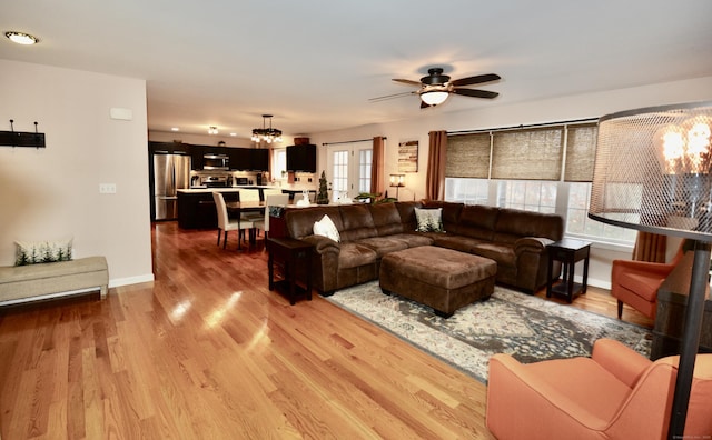 living area featuring ceiling fan with notable chandelier, light wood finished floors, and baseboards