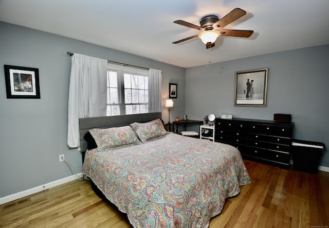 bedroom featuring a ceiling fan, visible vents, baseboards, and wood finished floors