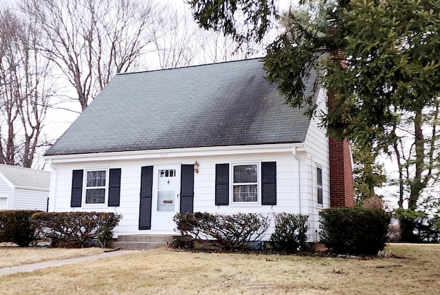 cape cod-style house featuring a chimney and a front lawn