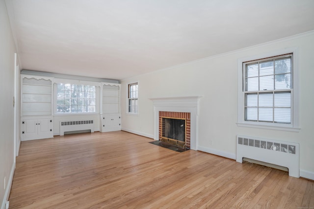 unfurnished living room featuring a brick fireplace, ornamental molding, light wood-type flooring, and radiator