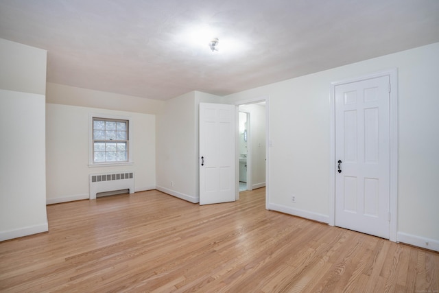 spare room featuring light wood finished floors, radiator heating unit, and baseboards