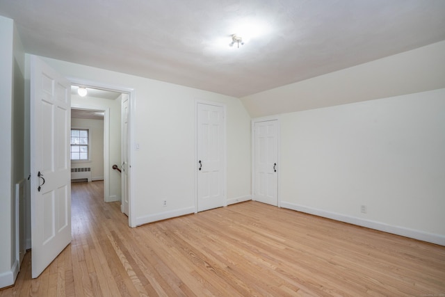 interior space with radiator heating unit, vaulted ceiling, baseboards, and light wood-style flooring