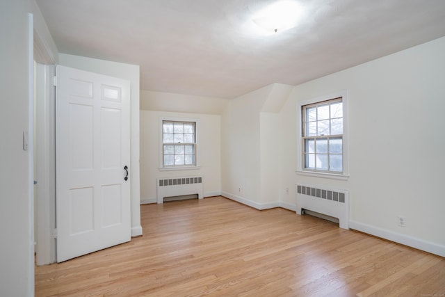 spare room featuring baseboards, radiator heating unit, and light wood-style floors