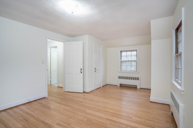 spare room featuring radiator, light wood-style flooring, and baseboards