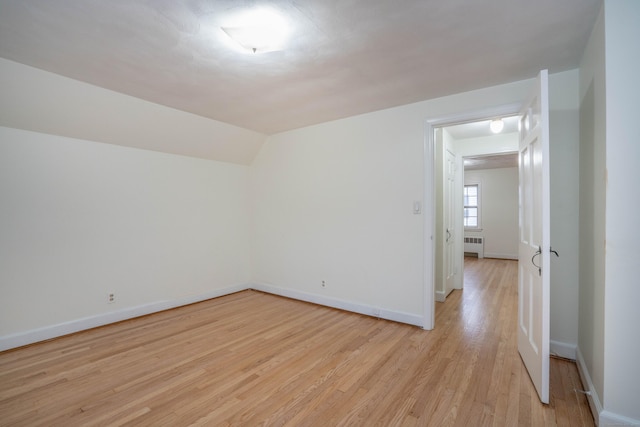 empty room with lofted ceiling, radiator heating unit, light wood-type flooring, and baseboards