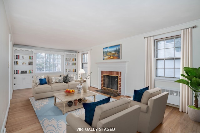 living room featuring a brick fireplace, light wood-style flooring, ornamental molding, and radiator heating unit