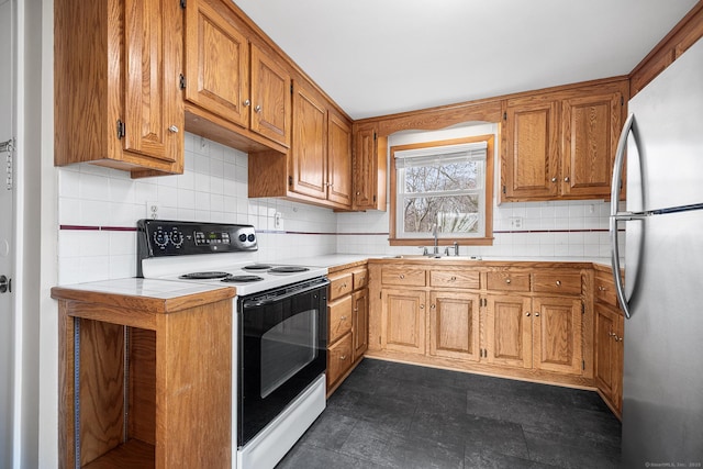 kitchen featuring light countertops, decorative backsplash, freestanding refrigerator, electric range, and a sink