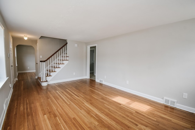 spare room featuring arched walkways, visible vents, stairway, wood finished floors, and baseboards