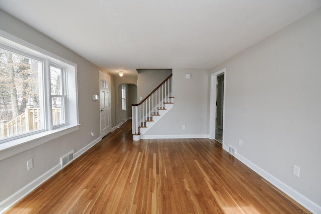 interior space featuring baseboards, visible vents, arched walkways, stairs, and light wood-type flooring