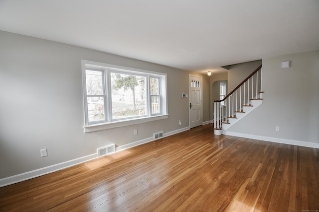 unfurnished living room with hardwood / wood-style flooring, baseboards, stairs, and visible vents