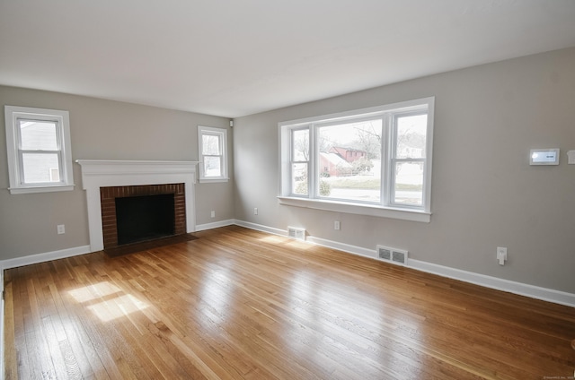 unfurnished living room featuring light wood-type flooring, a brick fireplace, baseboards, and visible vents