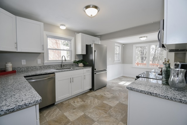 kitchen featuring stainless steel appliances, a sink, white cabinetry, wainscoting, and light stone countertops