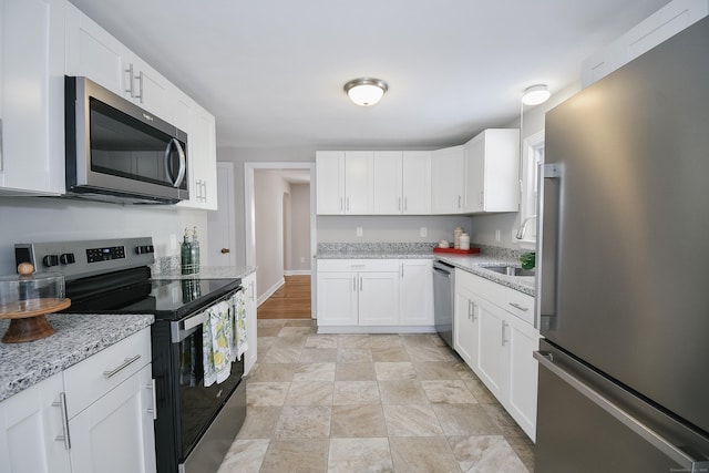 kitchen featuring stainless steel appliances, a sink, light stone countertops, and white cabinets