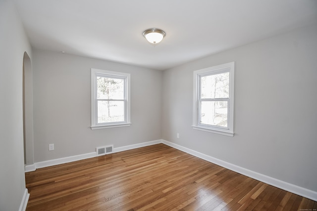 unfurnished room featuring hardwood / wood-style flooring, baseboards, visible vents, and arched walkways