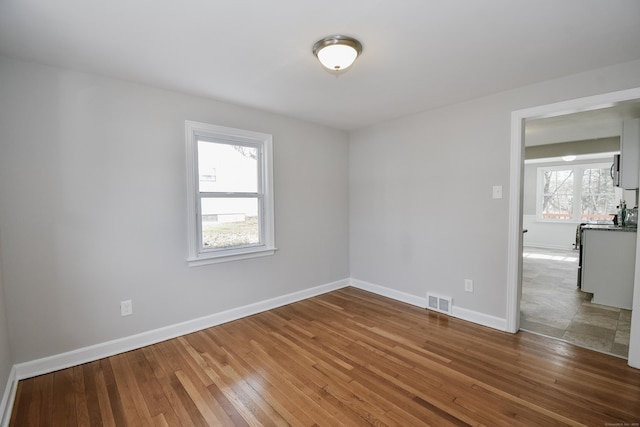 empty room featuring visible vents, hardwood / wood-style flooring, and baseboards