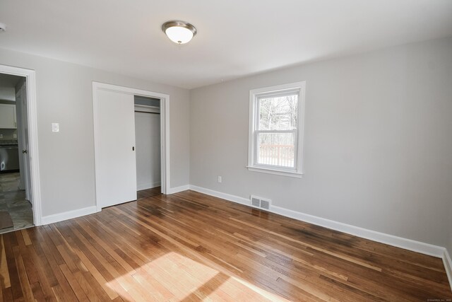 unfurnished bedroom with wood-type flooring, a closet, visible vents, and baseboards