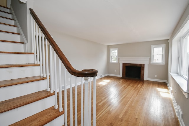 staircase with a brick fireplace, wood finished floors, and baseboards