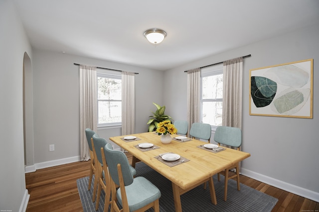 dining area featuring arched walkways, wood finished floors, and baseboards