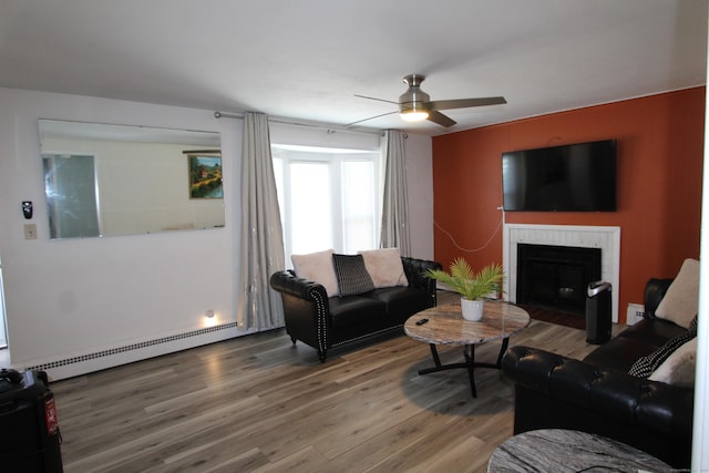 living room with a ceiling fan, a brick fireplace, baseboard heating, and wood finished floors