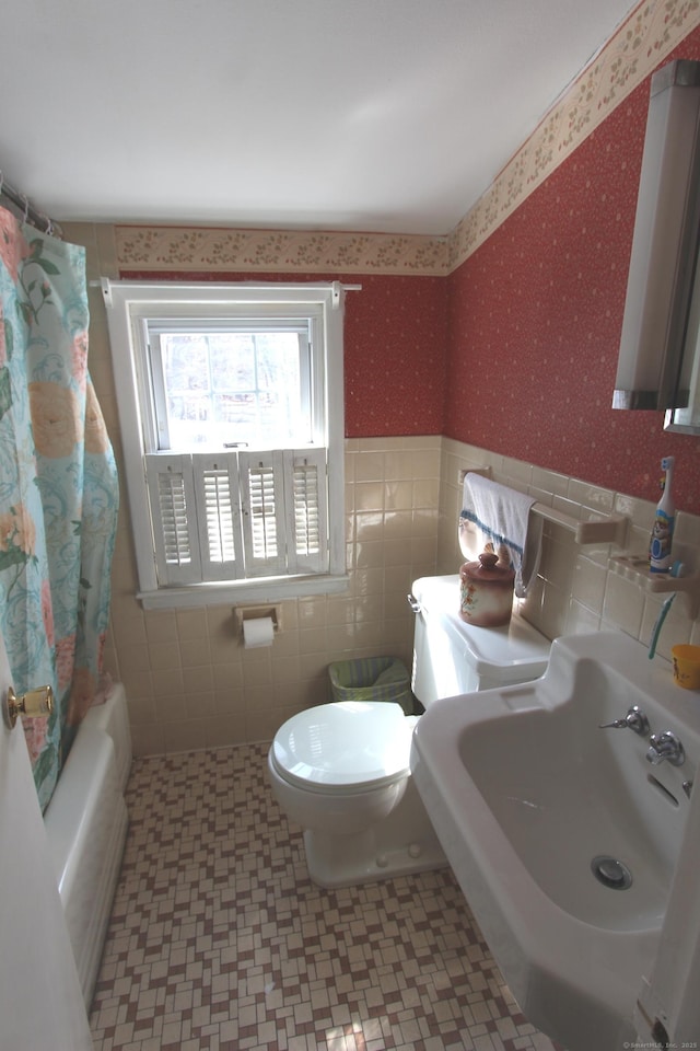 bathroom featuring toilet, a wainscoted wall, a sink, tile walls, and wallpapered walls