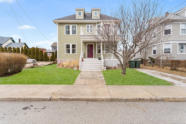 traditional style home featuring a front lawn, a porch, a balcony, and a shingled roof