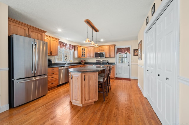 kitchen with appliances with stainless steel finishes, dark countertops, a center island, and light wood-style flooring