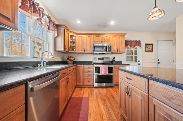 kitchen featuring a sink, appliances with stainless steel finishes, light wood-type flooring, brown cabinetry, and glass insert cabinets