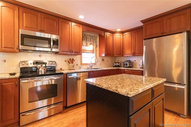 kitchen with a sink, appliances with stainless steel finishes, backsplash, light stone countertops, and light wood finished floors