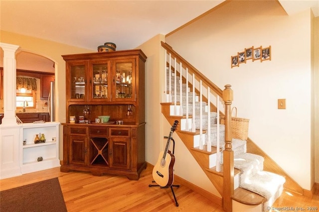 bar with light wood-style flooring, a sink, stairway, fridge, and decorative columns