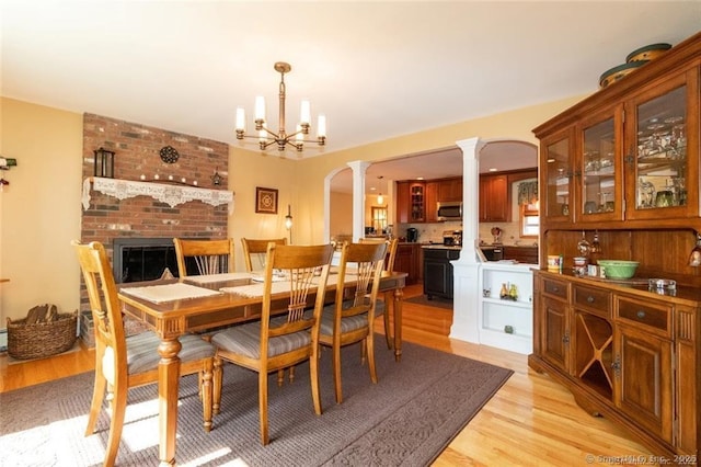 dining space with ornate columns, light wood-style flooring, a chandelier, and arched walkways