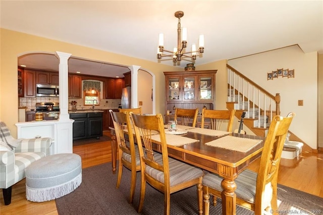 dining area featuring arched walkways, light wood finished floors, a notable chandelier, and ornate columns