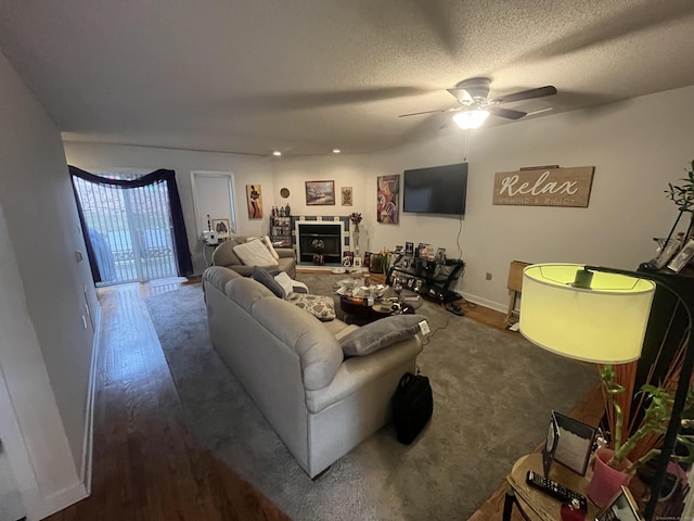 living room featuring a textured ceiling, a fireplace, wood finished floors, a ceiling fan, and baseboards