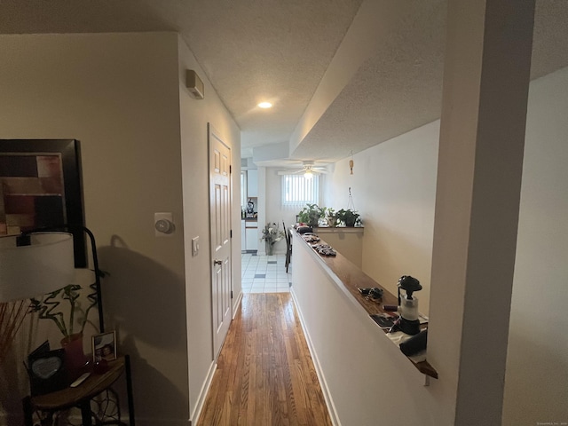 hallway featuring a textured ceiling, light wood finished floors, and baseboards